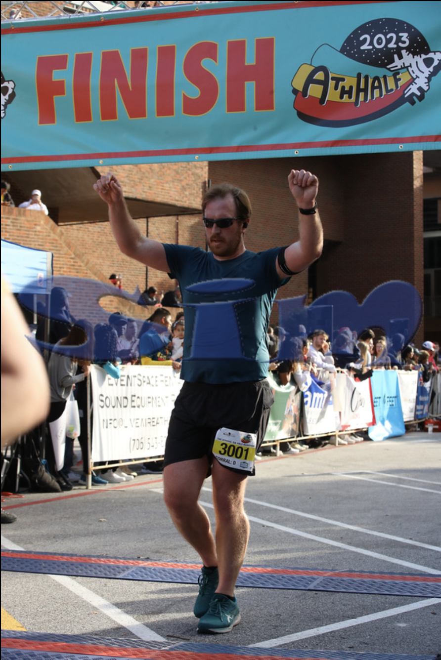 A photo of me crossing the finish line at Ath Half 2023 this past October, holding up my arms in exhausted triumph.