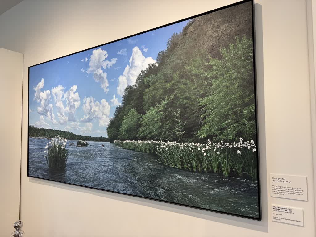 Oil-on-canvas painting of a riverbed with lots of greenery both in and out of the water, hanging on the wall at the local Botanical Gardens.